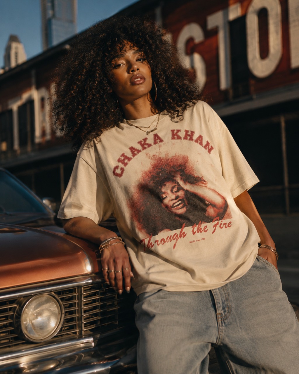 Model wearing the cream Chaka Khan Through the Fire tee beside a classic car