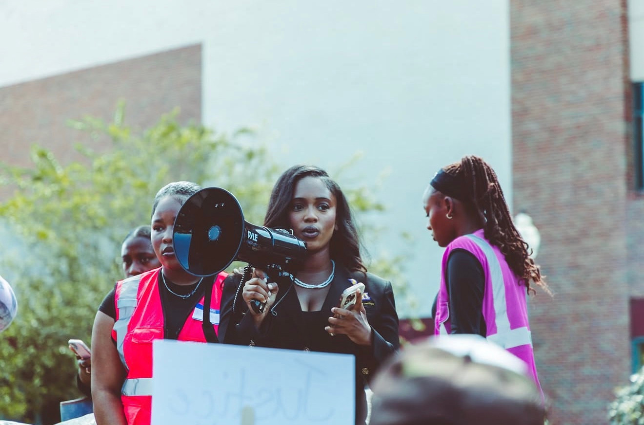 A rally participant holds a megaphone and a phone while others stand beside her